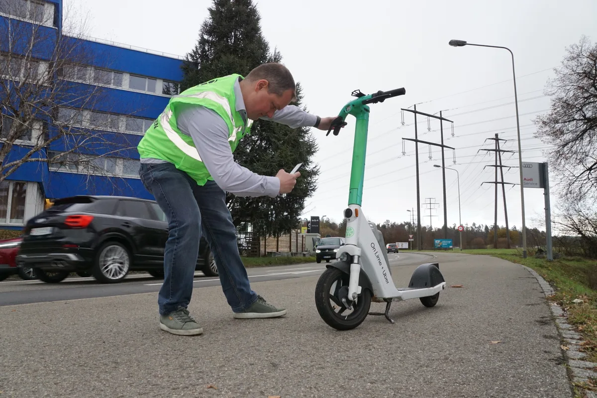 Ein Mann mit gelber Weste fotografiert einen kaputten Reflektor an einem Lime-Fahrzeug. 